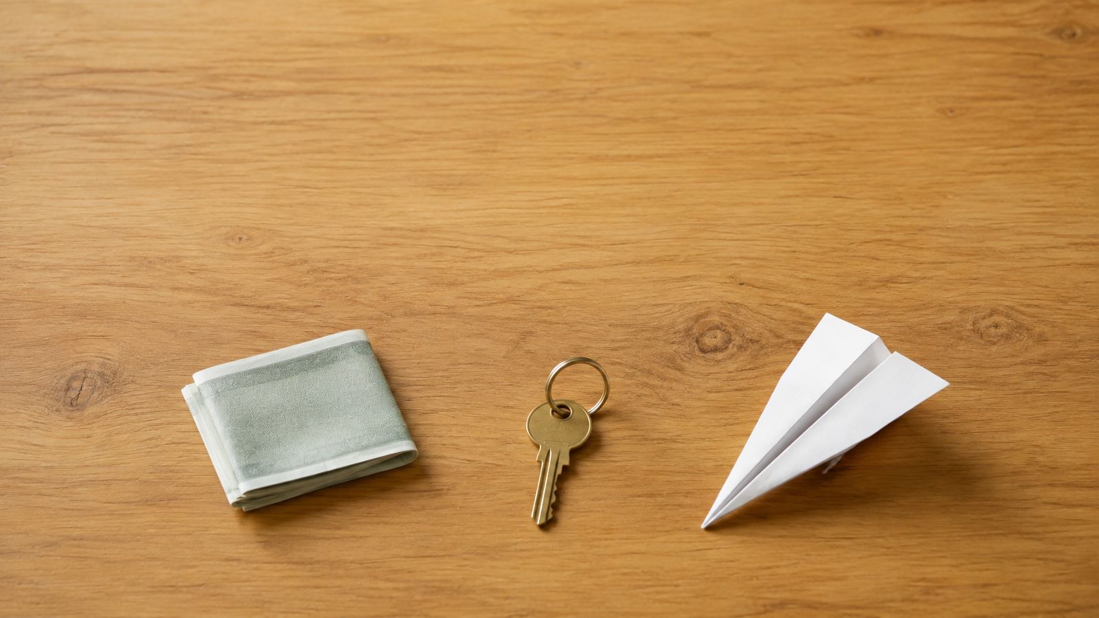 Folded bills, a brass door key, and a paper airplane laid out on a wooden table